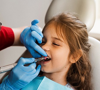 Dentist in blue gloves polishing girl’s teeth