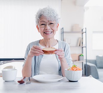 Older woman eating lunch and smiling with dentures