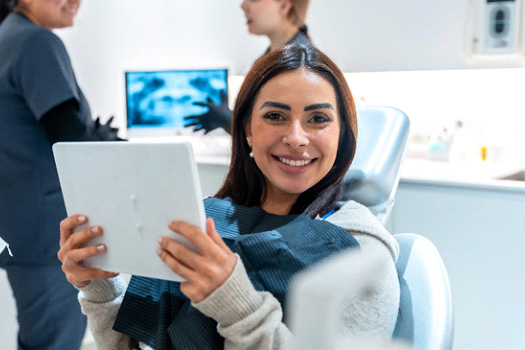 Patient smiling while holding mirror in treatment chair