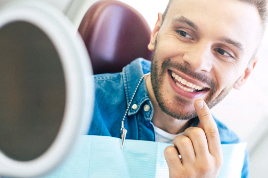 Man smiling at reflection in handheld mirror