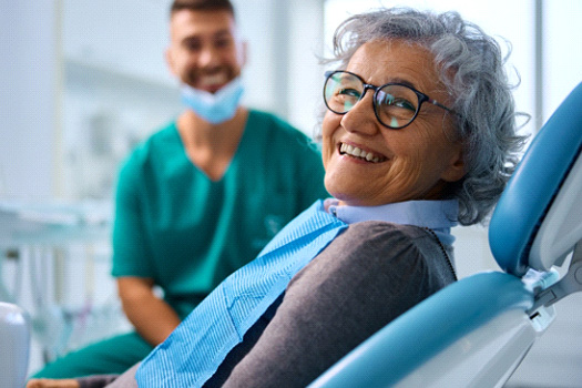 Woman with black glasses smiling while sitting in treatment chair
