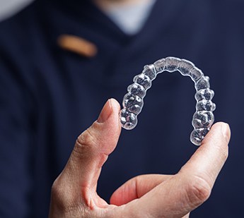 Dentist in navy scrubs holding clear aligner