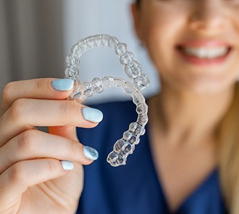 Woman with light blue nails holding two clear aligners