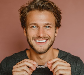Man smiling holding clear aligner with brown background