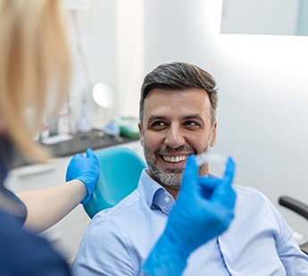Man in dental chair smiling at dentist holding clear aligner